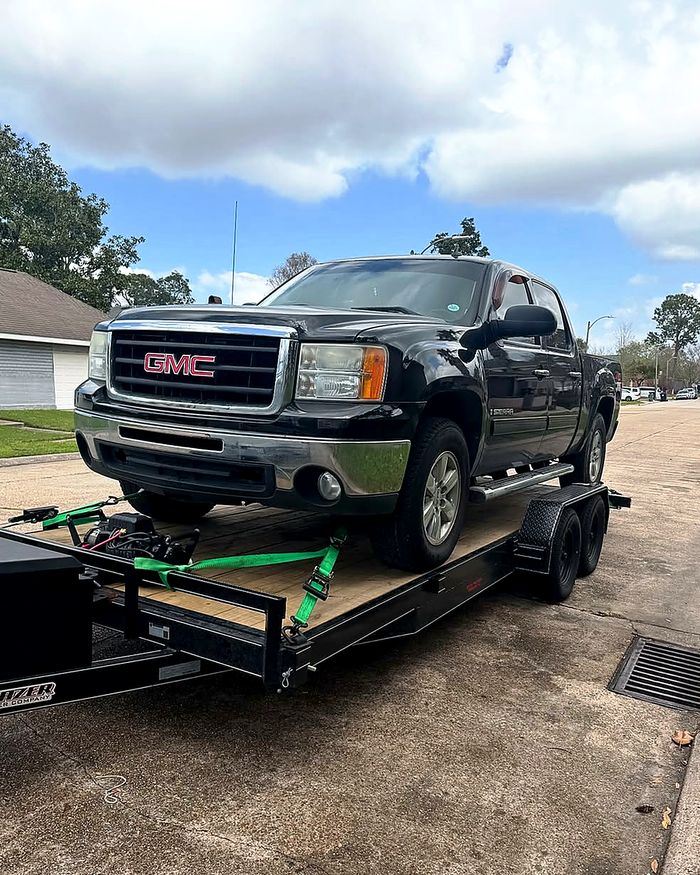 A black GMC Sierra pickup loaded and strapped on Rik's Towing trailer in a residential driveway.